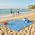 Blue and white sand-free beach blanket laid out on sunny beach with ocean waves